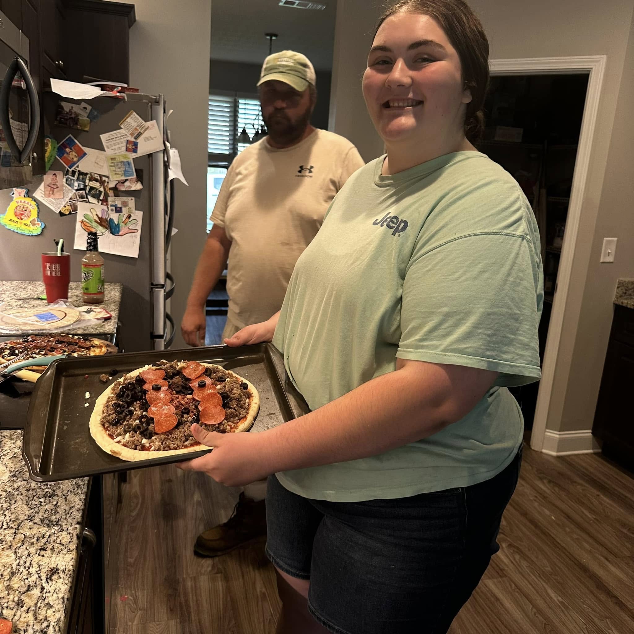 One of the kids and her dad in the kitchen with a pizza they made together.